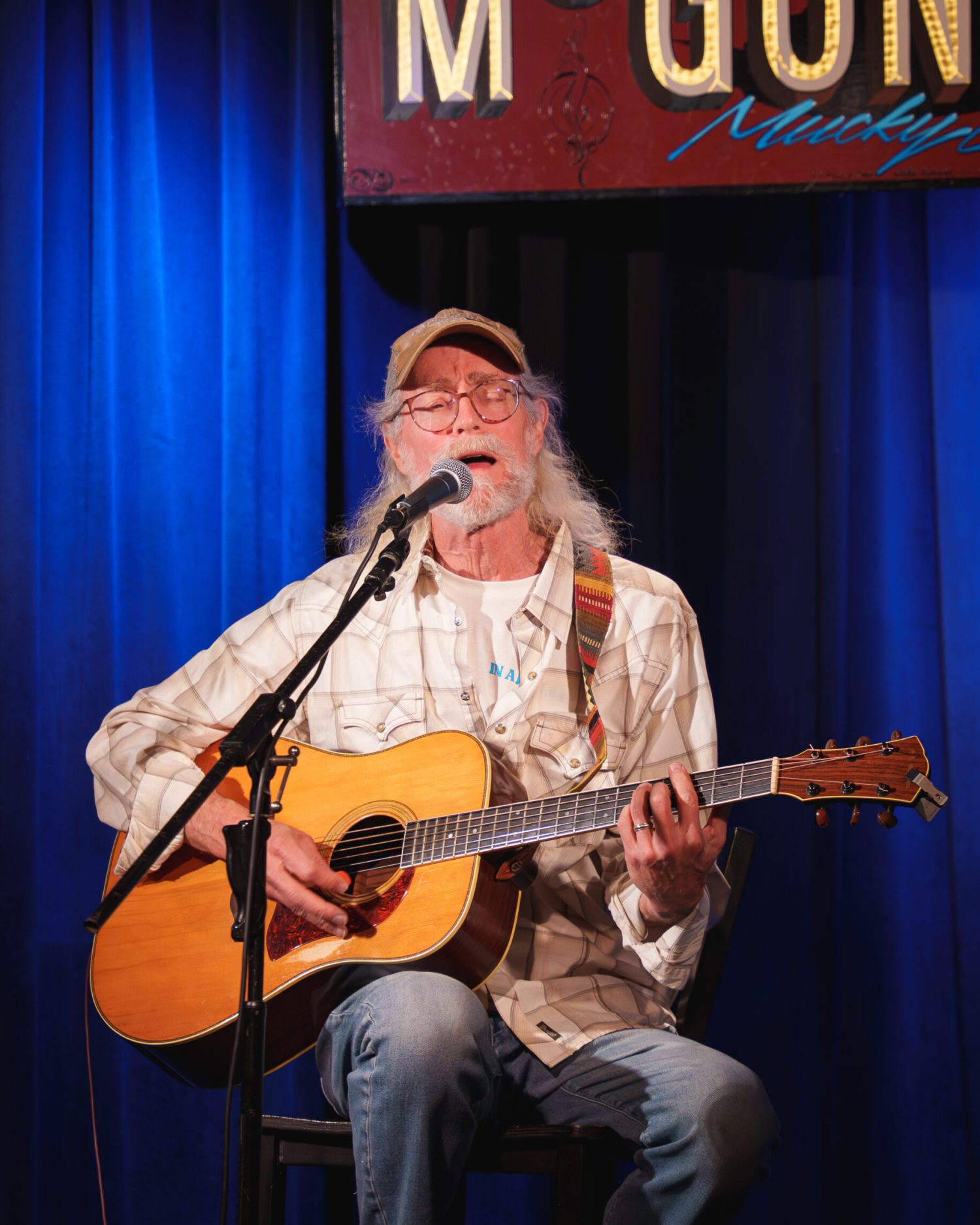 Live performance photography during a live performance in Houston Texas by Minuit Studios music photography live performance photography of a country styled with white beard and hair singer playing the accoustic guitar during an open mic concert at Houston Mucky Duck - Minuit studios music concert musical artists imagery